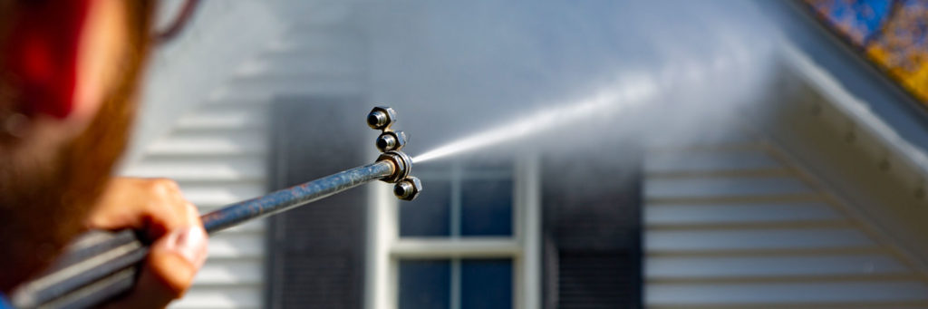 Power washing technician using safe pressure to wash white vinyl siding