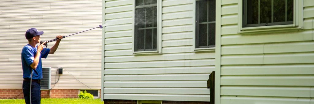 Power washing technician using wand to soft wash vinyl siding