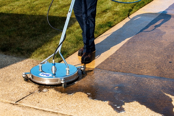 Power washing technician using circular surface cleaner to safely wash a concrete surface
