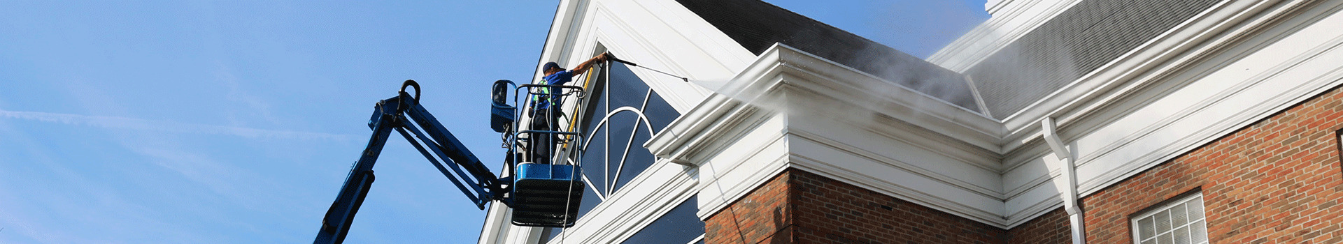 Perfect Power Wash employee on a lift power washing the top of a brick commercial building