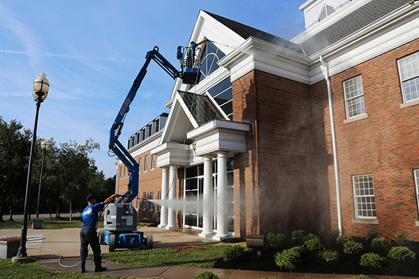 Perfect Power Wash employee on a lift power washing the talk of a brick commercial building